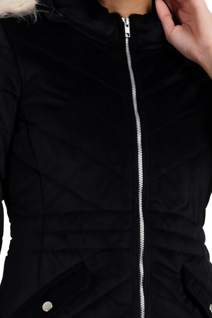 A cropped shot of a woman wearing Trufit’s black velvet quilted jacket with a zip closure, removable hood with faux fur trim, high neck, and slash pockets with her left hand on her neck.