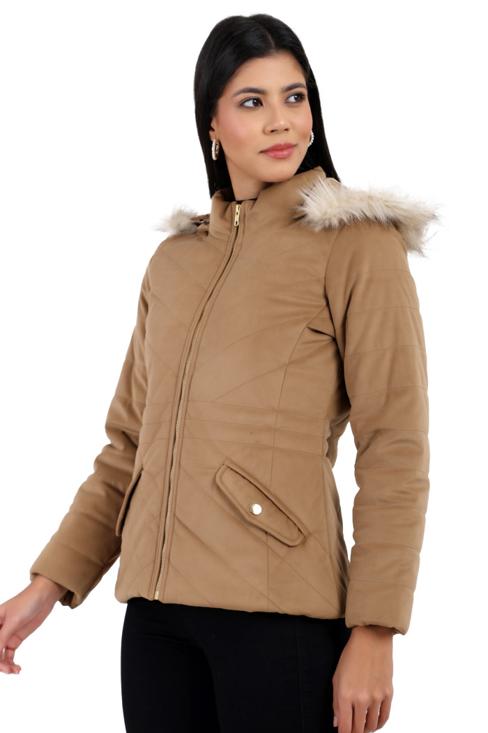 A woman in a standing side pose is wearing Coatsnmore’s coffee velvet quilted jacket with a high neck, zip closure, removable hood with faux fur trim, slash pockets, and blue jeans.