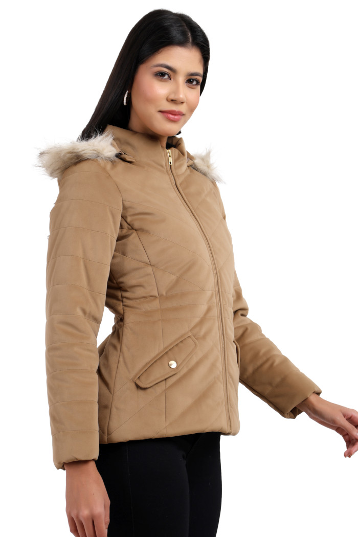 A woman in a standing pose, wearing Coatsnmore’s coffee velvet quilted jacket with a high neck, zip closure, removable hood with faux fur trim, slash pockets and blue jeans, with her right hand on the waist.