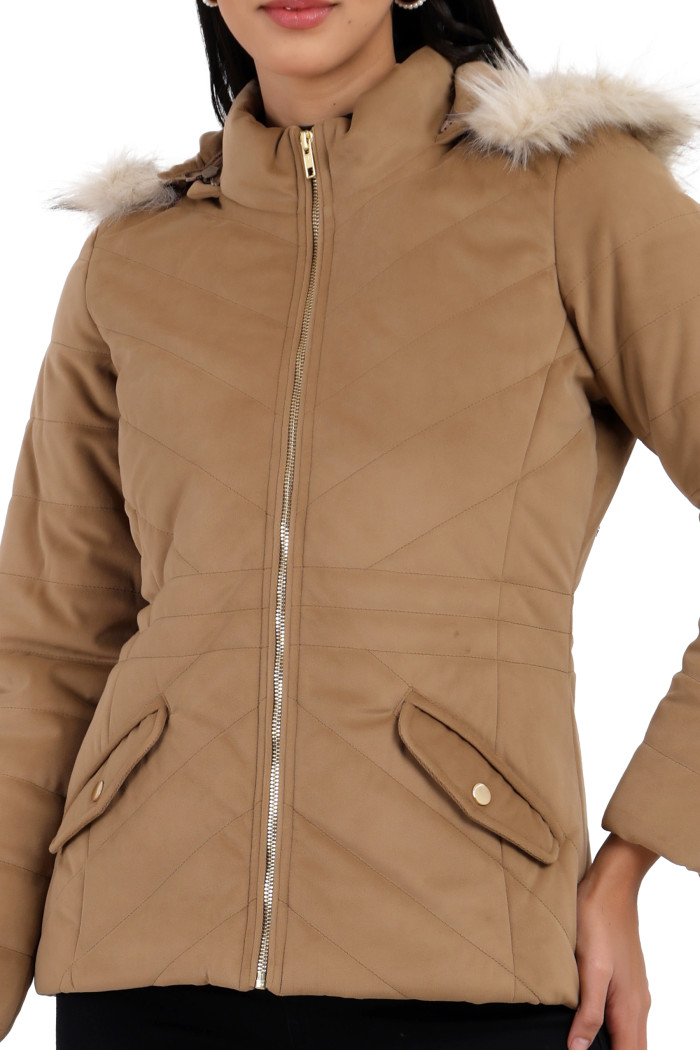 A cropped image of a woman wearing Coatsnmore’s coffee velvet quilted jacket with a high neck, zip closure, removable hood with faux fur trim, and slash pockets with her right hand on her waist.