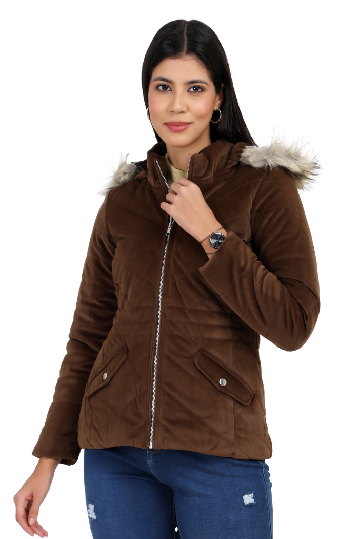 A woman in a standing pose, wearing Coatsnmore’s coffee velvet quilted jacket with a high neck, zip closure, removable hood with faux fur trim, slash pockets and blue jeans while holding the jacket's collar with her left hand.