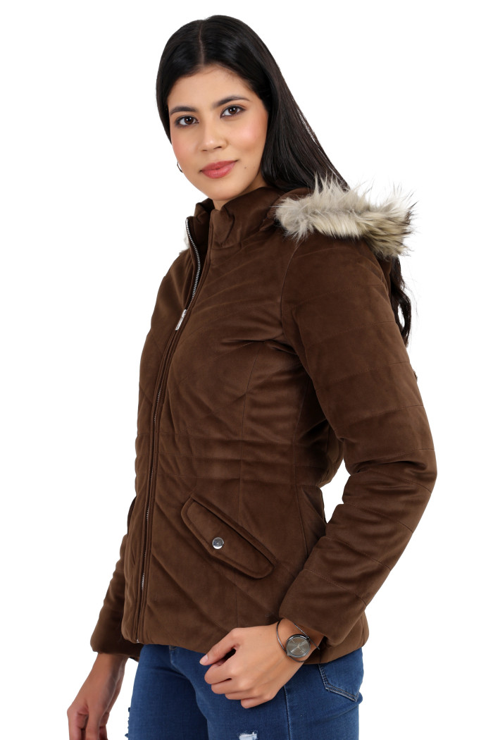 A woman in a standing side pose is wearing Coatsnmore’s coffee velvet quilted jacket with a high neck, zip closure, removable hood with faux fur trim, slash pockets, and blue jeans.