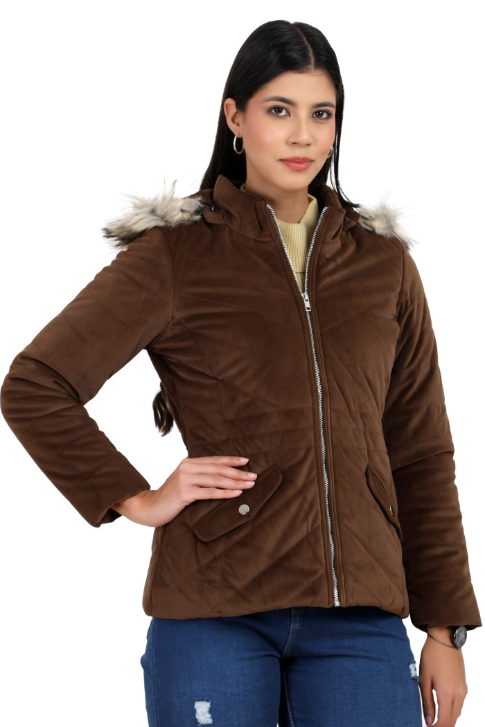 A woman in a standing pose, wearing Coatsnmore’s coffee velvet quilted jacket with a high neck, zip closure, removable hood with faux fur trim, slash pockets and blue jeans, with her right hand on the waist.