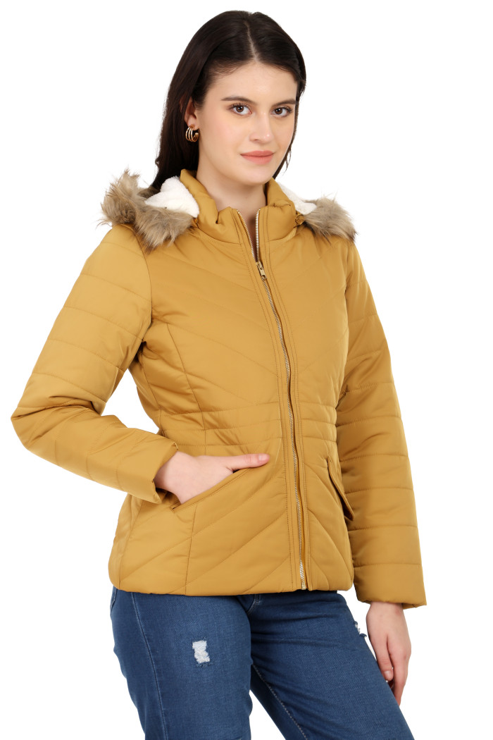 A woman is giving a standing side pose wearing Coatsnmore’s casual jacket in mustard colour with a textured pattern, slash placket pockets, a zip closure, a detachable hood and blue jeans with her right hand in the pocket.