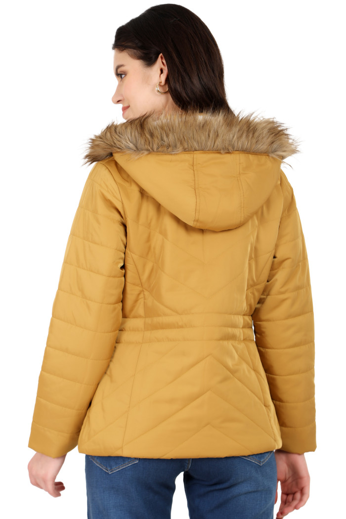 A back pose of a standing woman, wearing Coatsnmore’s coatsnmore’s casual jacket in mustard colour with a textured pattern, a removable hood and blue jeans.