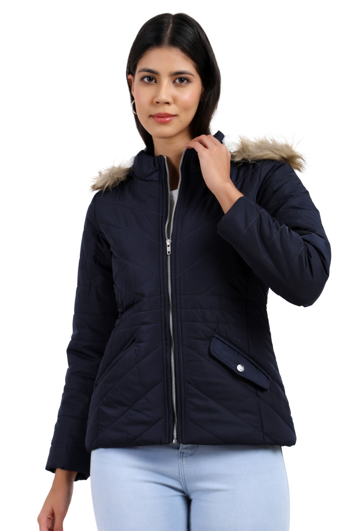 A woman is giving a standing side pose wearing Coatsnmore’s casual jacket in navy colour with a textured pattern, slash placket pockets, a zip closure, a detachable hood and blue jeans while holding the collar with her left hand.