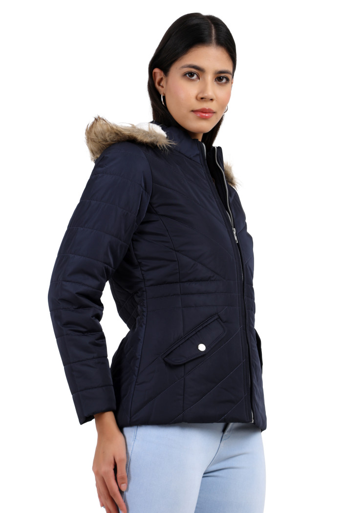 A woman is giving a standing side pose wearing Coatsnmore’s casual jacket in navy colour with a textured pattern, slash placket pockets, a zip closure, a detachable hood and blue jeans with her left hand in the pocket.