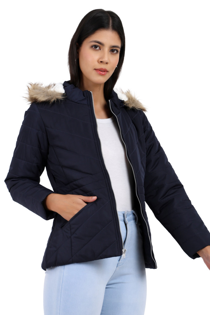 A standing pose of a woman wearing Coatsnmore’s casual jacket in navy colour with a textured pattern, slash placket pockets, a zip closure, a detachable hood and blue jeans with her right hand in a pocket.