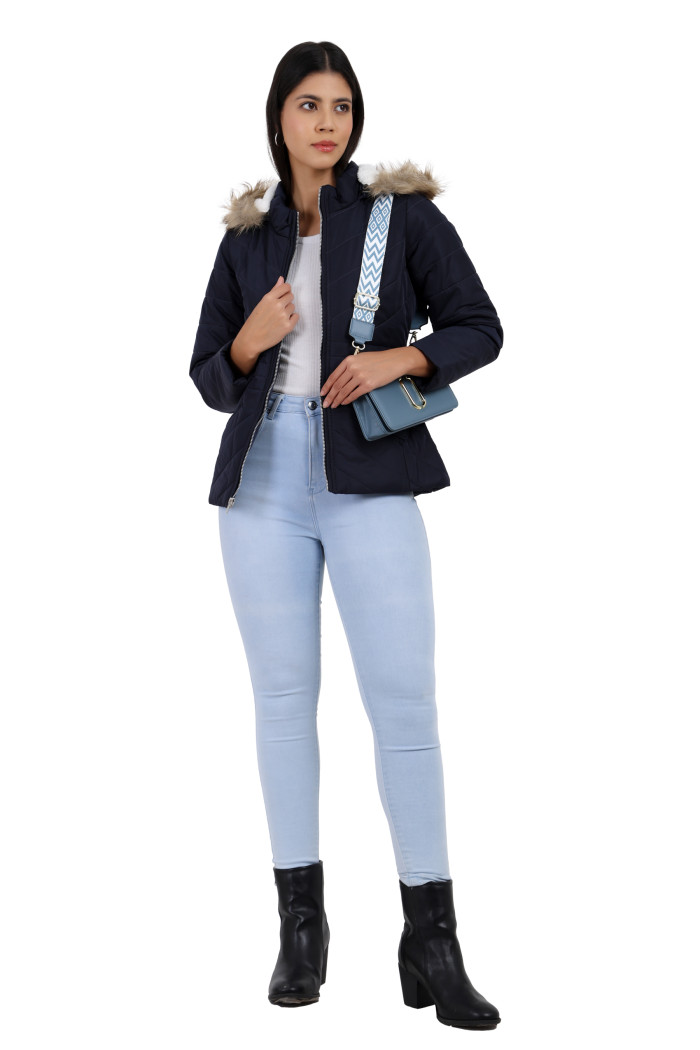 A woman is giving a standing pose wearing Coatsnmore’s casual jacket in navy colour with a textured pattern, slash placket pockets, a zip closure, a detachable hood and blue jeans while holding a slinging bag.