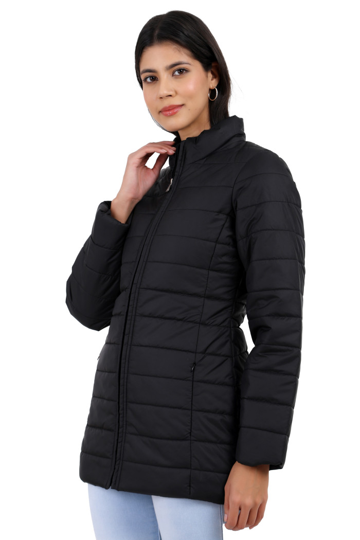 A woman in a standing side pose is wearing Trufit’s black quilted jacket with a mandarin collar, zip closure, side pockets with concealed zippers, and blue jeans and holding her collar with her right hand.