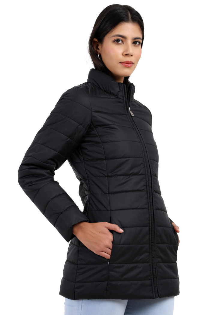 A woman in a standing side pose is wearing Trufit’s black quilted jacket with a high neck collar, zip closure, side pockets with concealed zippers, and blue jeans, and her hands are in the pocket.