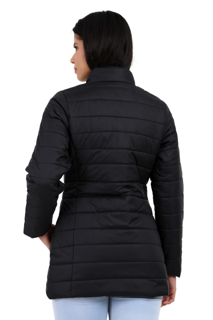 A back pose of a standing woman wearing Trufit’s black quilted jacket with a stand collar and blue jeans.