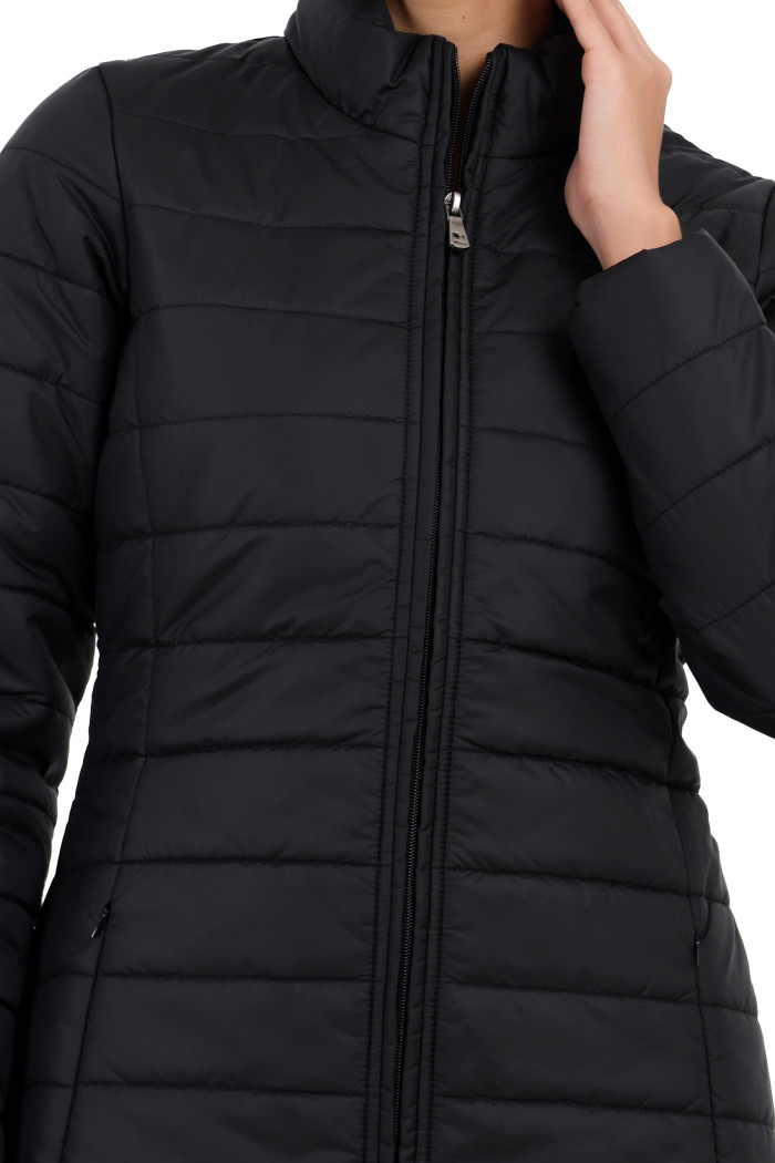 A cropped image of a woman wearing Trufit’s black quilted jacket with a high neck collar, zip closure, side pockets, and concealed zippers, and her left hand is on her neck.