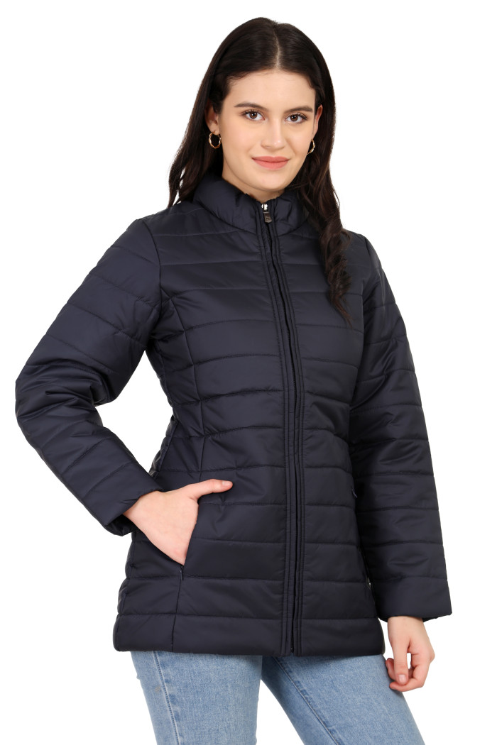 A woman in a standing pose is wearing Coatsnmore’s navy quilted jacket with a stand collar, zip closure, side pockets with concealed zippers, and blue jeans, and her right hand is in the pocket.