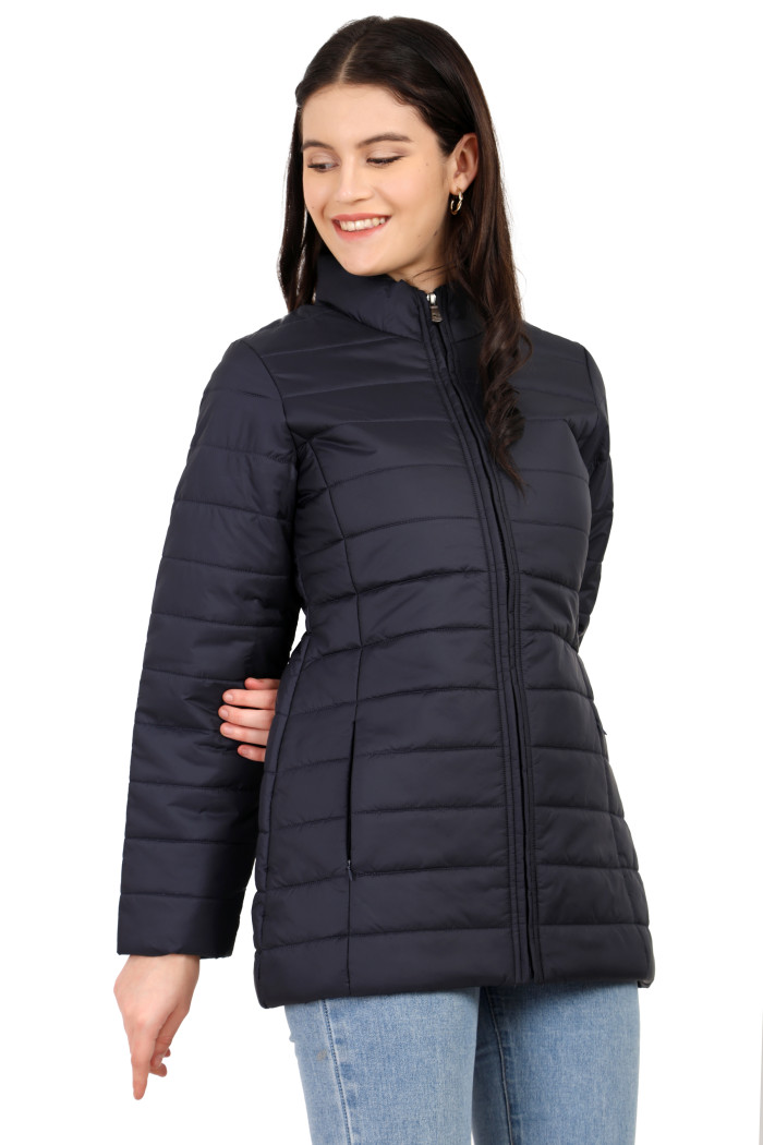 A woman in a standing side pose is wearing Coatsnmore’s navy quilted jacket with a high neck collar, zip closure, side pockets, concealed zippers, and blue jeans.