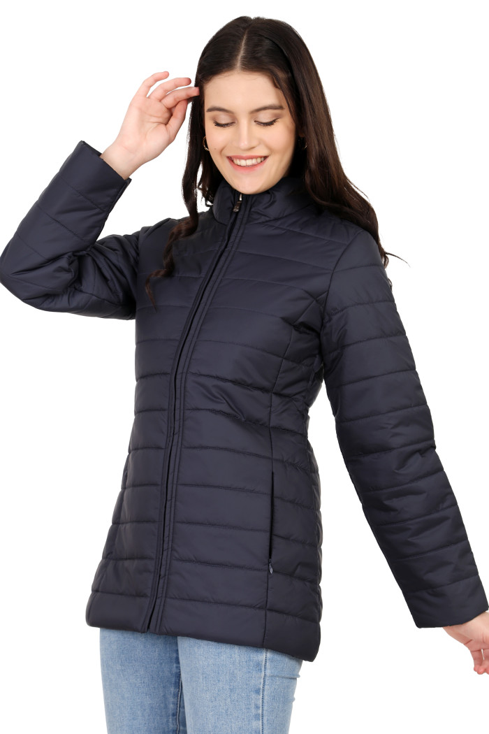 A woman in a standing side pose is wearing Coatsnmore’s navy quilted jacket with a mandarin collar, zip closure, side pockets, concealed zippers, and blue jeans.