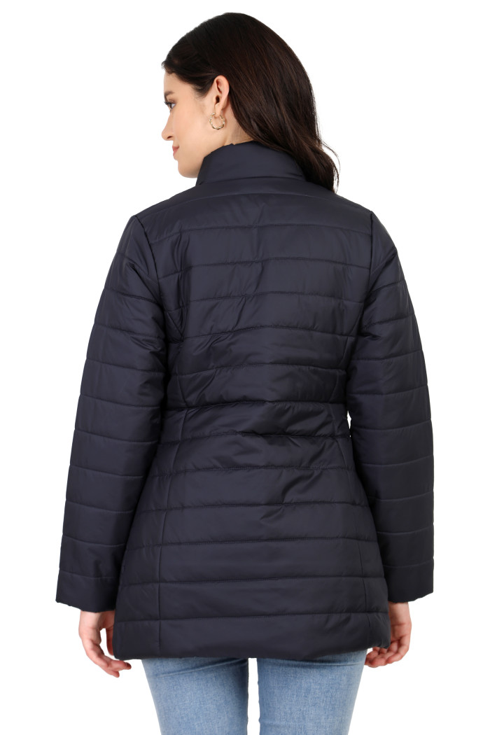 A back pose of a standing woman wearing Coatsnmore’s navy quilted jacket and blue jeans.