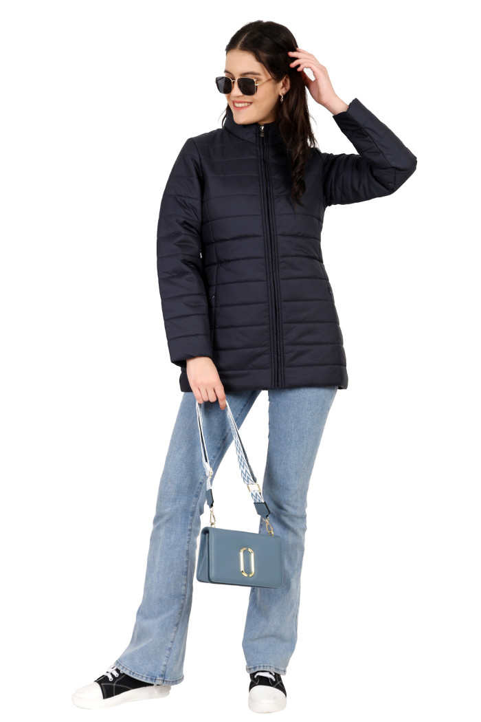 A woman in a standing pose in black shades is holding a clutch and wearing Coatsnmore’s navy quilted jacket with a high neck collar, zip closure, side pockets with concealed zippers, and blue jeans.