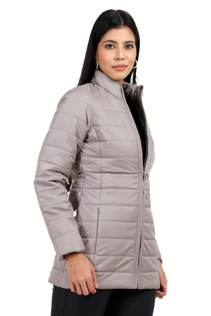 A woman in a standing side pose is wearing Trufit’s stone quilted jacket with a high neck collar, zip closure, side pockets with concealed zippers, and black jeans.