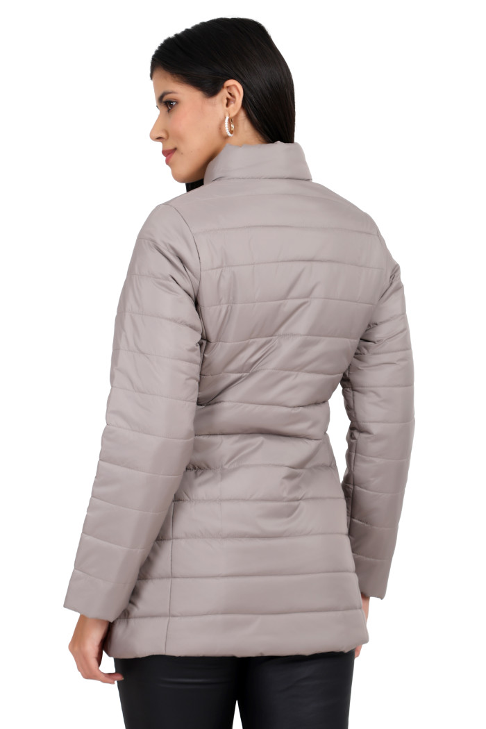 A back pose of a standing woman wearing Trufit’s stone quilted jacket and black jeans.