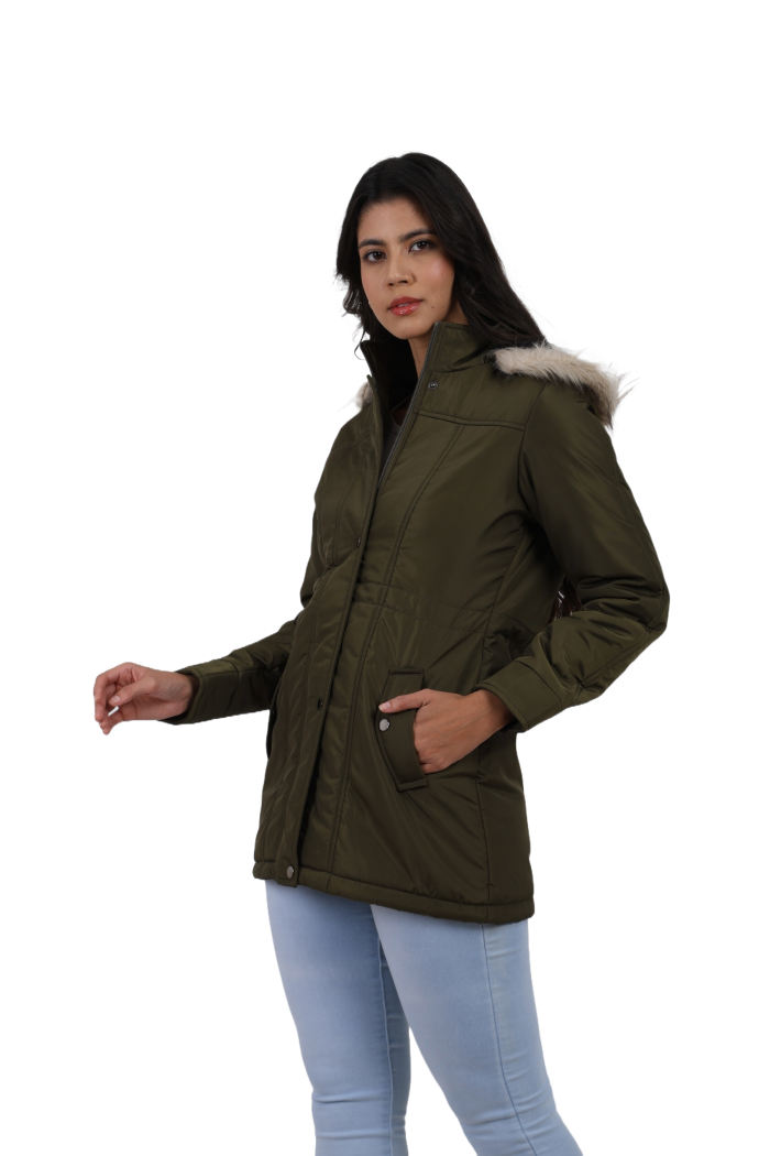 A woman is giving a standing left side pose, wearing Coatsnmore’s olive quilted parka jacket with a detachable hood, zip closure, button placket, side pockets and quilted pattern and blue jeans with left hand in pocket.