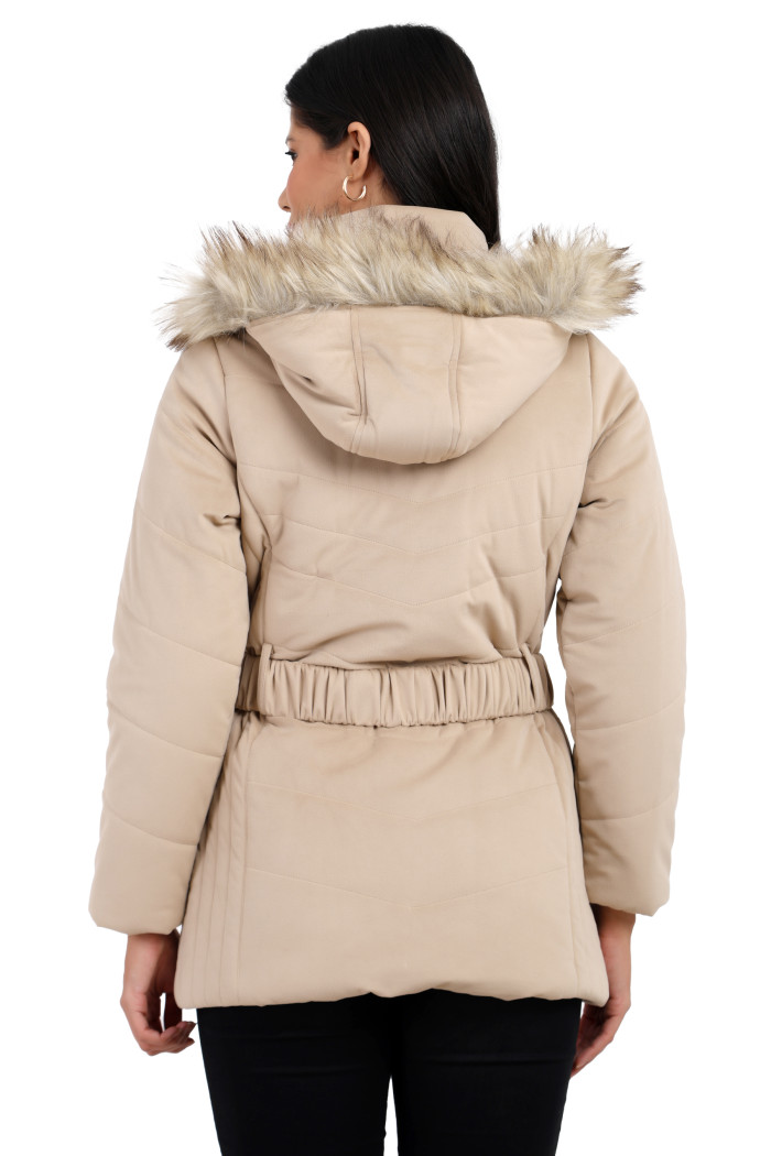 The back view of a standing woman wearing Coatsnmore’s beige velvet quilted jacket with a removable hood and adjustable waistband paired with black jeans.