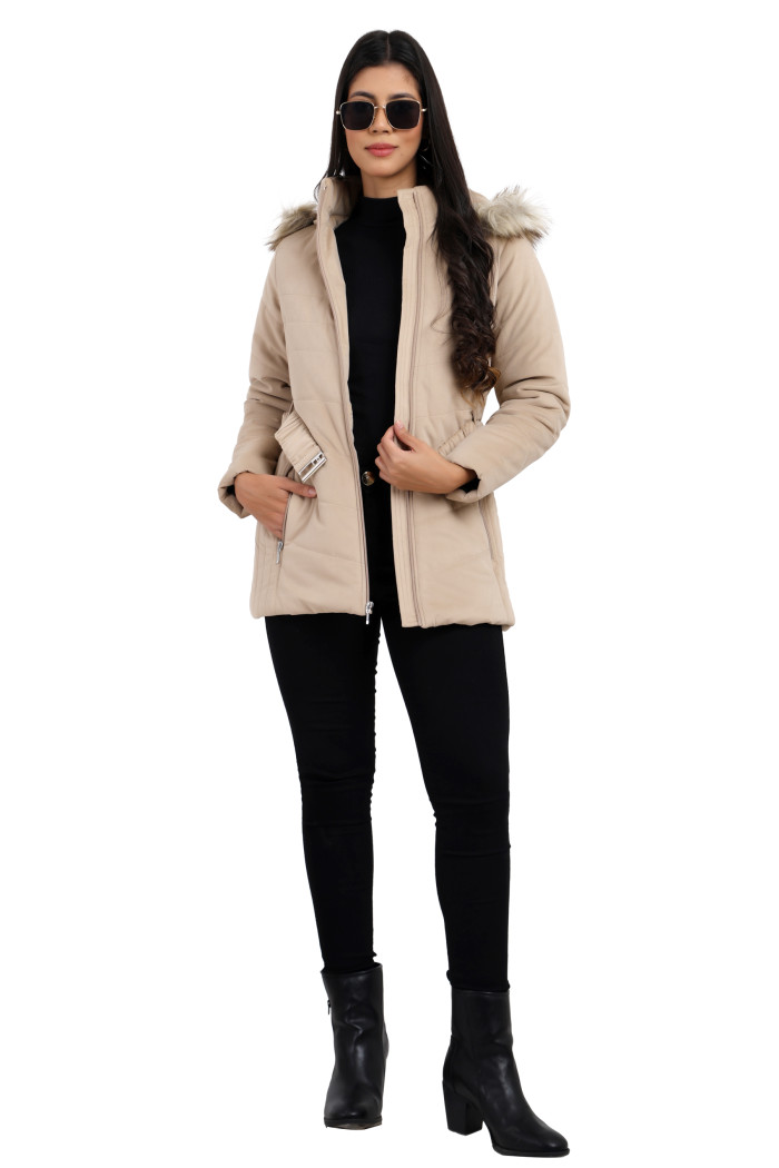 A woman in a standing pose, styled in Coatsnmore’s beige velvet quilted jacket featuring stand collar, removable hood, adjustable waistband zip closure, concealed zippered pockets and jeans and holding the jacket with left hand and right hand in pocket.