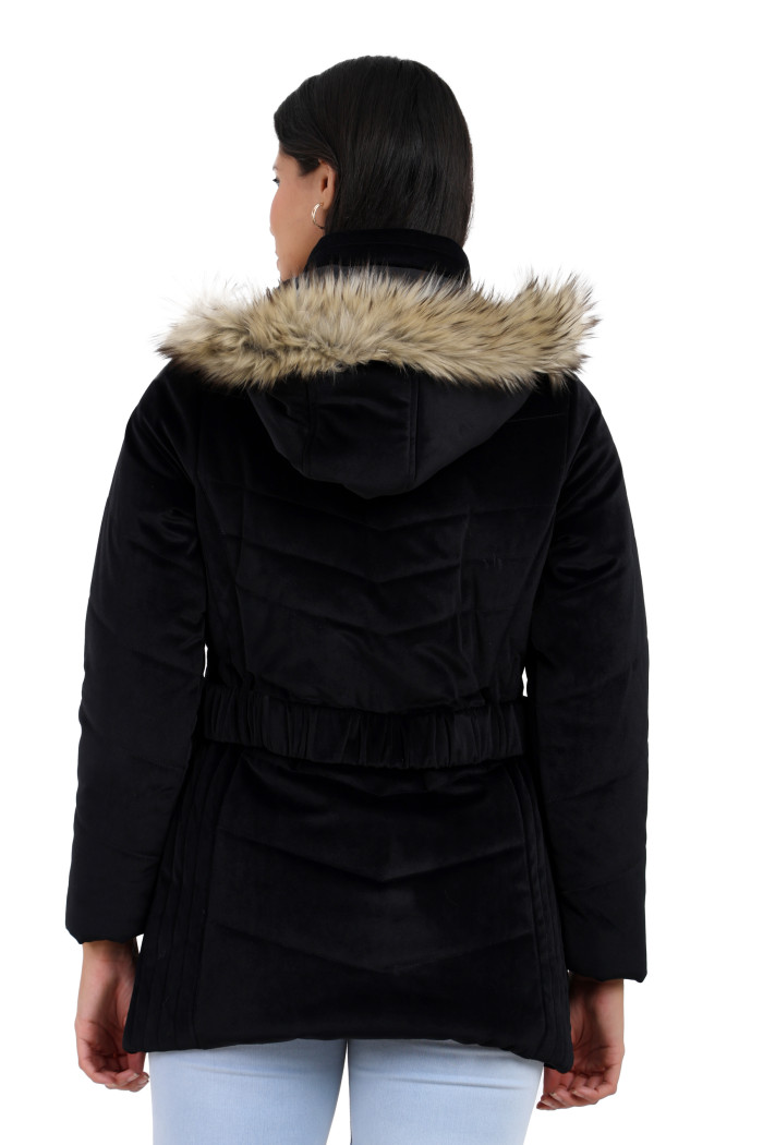 The back view of a standing woman wearing Coatsnmore’s black velvet quilted jacket with a removable hood paired with blue jeans.