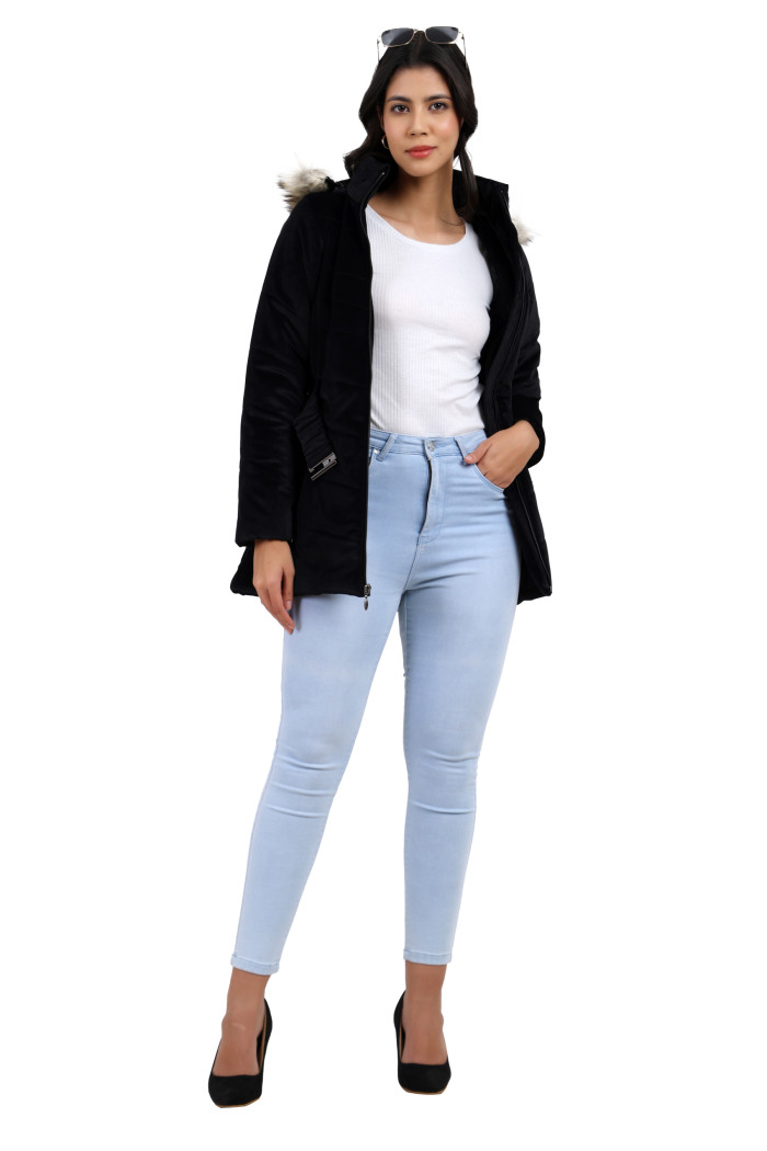 A woman stands confidently with black sunglasses on her head, styled in Coatsnmore’s black velvet quilted jacket featuring a mandarin collar, removable hood, adjustable waistband zip closure, concealed zippered side pockets and blue jeans.