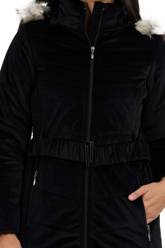 A cropped view of a woman in Coatsnmore’s black velvet quilted jacket, featuring a mandarin collar, removable hood, adjustable waistband zip closure, and concealed zippered side pockets, with her left hand in the pocket.