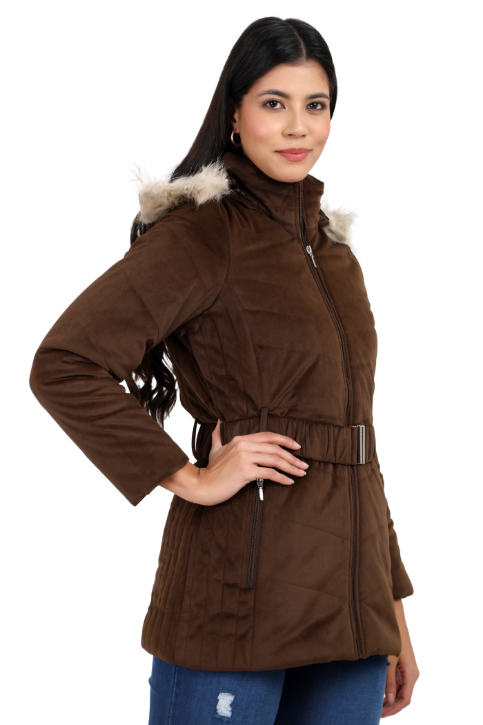 A woman in a side pose showcases Coatsnmore’s coffee velvet quilted jacket, featuring a mandarin collar, removable hood, adjustable waistband zip closure, concealed zippered side pockets, and blue jeans with her right hand on her waist.