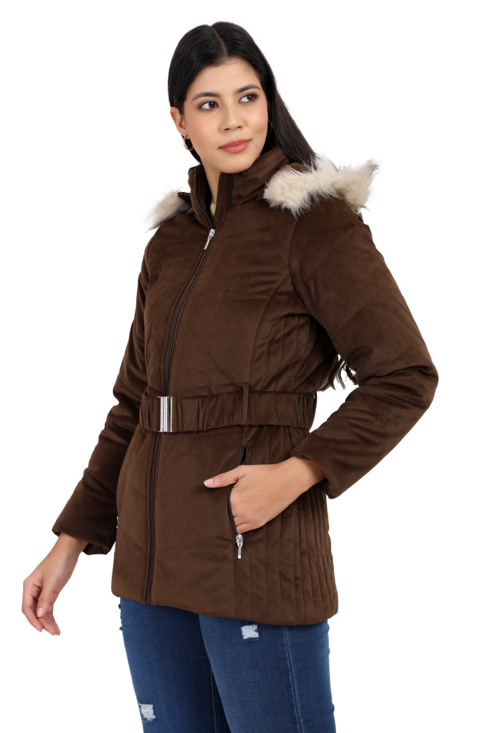 A side profile of a woman standing highlights Coatsnmore’s coffee velvet quilted jacket, featuring a mandarin collar, removable hood, adjustable waistband zip closure, concealed zippered side pockets and blue jeans with her left hand in the pocket.