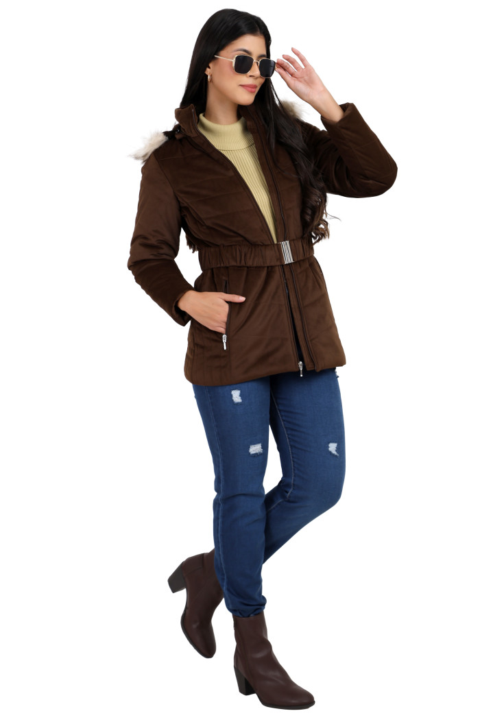 A woman in a standing pose, styled in Coatsnmore’s coffee velvet quilted jacket featuring a stand collar, removable hood, waistband, zip closure, concealed zippered pockets and jeans and holding her shades with her left hand and right hand in the pocket.