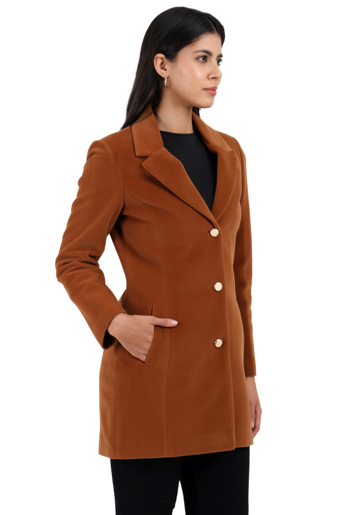 A woman is holding a standing side pose, wearing Coatsnmore’s rust Semi-Long Velvet coat with a lapel collar, button closure, side pockets, and black jeans with her right hand in the pocket.