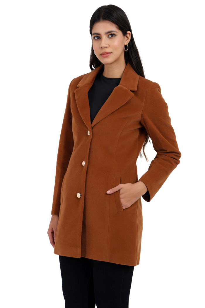 A woman is giving a standing side pose, wearing Coatsnmore’s rust Semi-Long Velvet coat with a lapel collar, button closure, side pockets and black jeans with her left hand in the pocket.