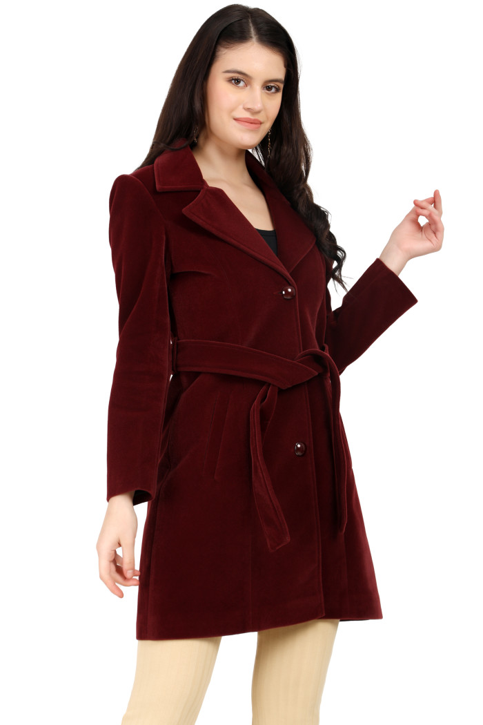 A woman is holding a standing side pose, wearing Trufit’s Long Wine Velvet coat with a lapel collar, button closure, belt, side pockets, and skin bell bottom.