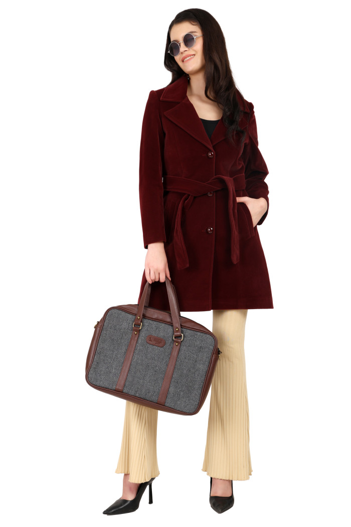 A standing pose of a woman in black shades, wearing Trufit’s Long wine Velvet coat with a lapel collar, button closure, belt, side pockets, and skin bell bottom and holding a bag from her left hand and her right hand in the pocket.