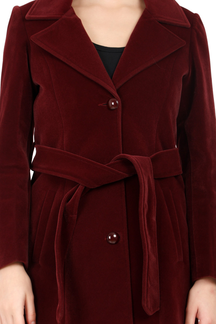 A cropped image of a woman wearing Trufit’s Long wine Velvet coat with a lapel collar, button closure, belt and side pockets.