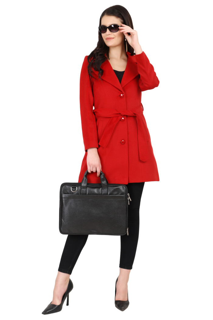 A woman holding her shades with her left hand stands elegantly in Coatsnmore’s long red tweed coat with a belt featuring a lapel collar, button-up design and side pockets and wearing black tights, holding a bag in her right hand.