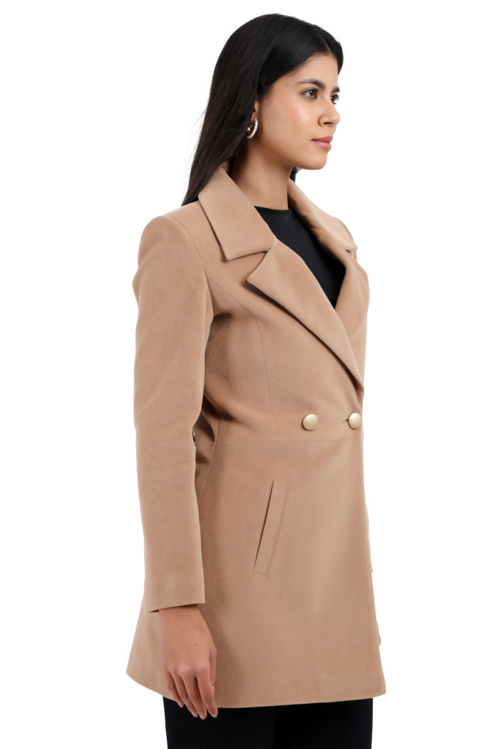 A standing side pose of a woman wearing Trufit’s double-breasted velvet coat in camel colour with a lapel collar, side pockets, button closure, and black jeans.