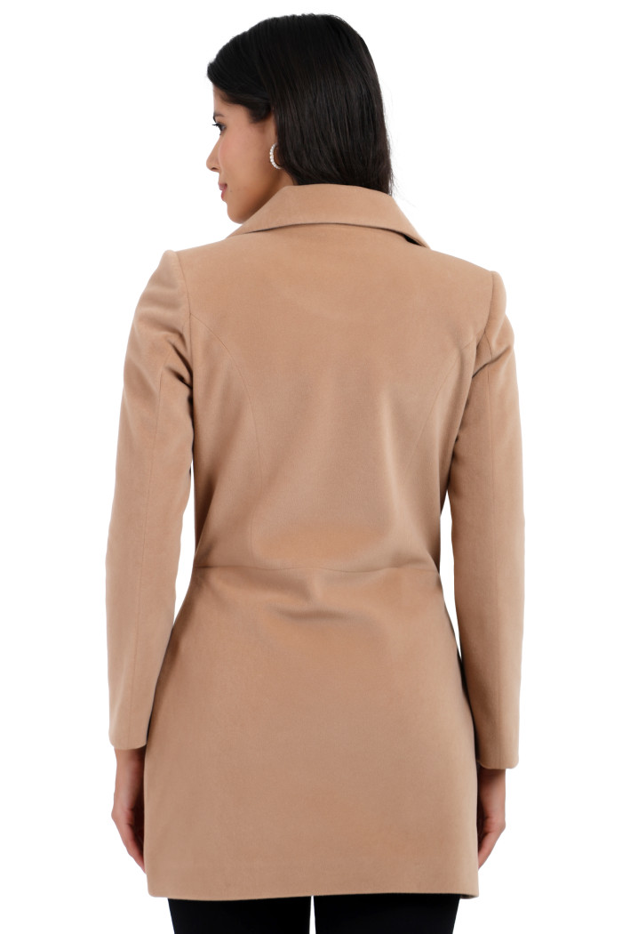 A back pose of a standing woman wearing Trufit’s double-breasted velvet coat in camel colour and black jeans.