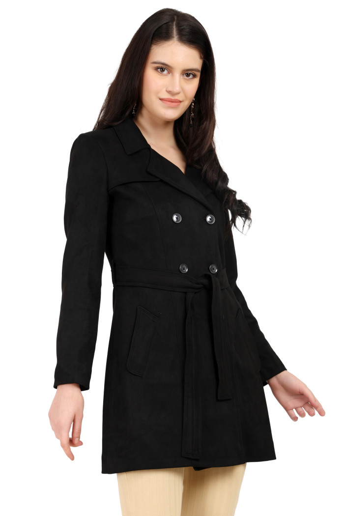 A woman is holding a standing side pose, wearing Coatsnmore’s black double-breasted trench coat with a lapel collar, button closure, belt, side pockets, and skin bell bottom.