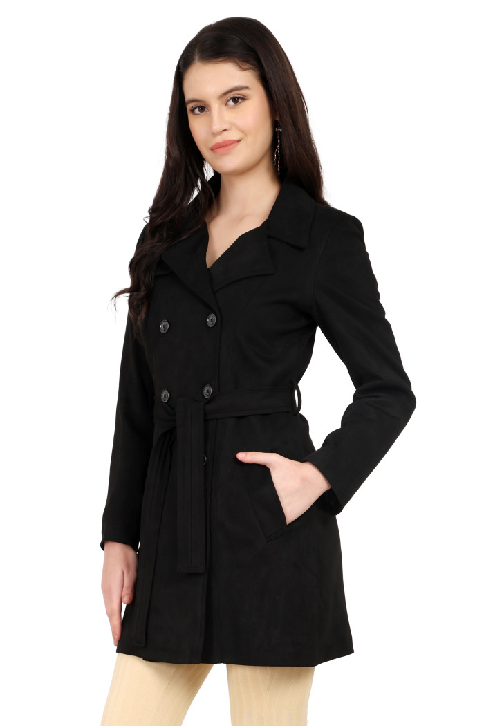 A woman is giving a standing side pose, wearing Coatsnmore’s black double-breasted trench coat with a lapel collar, button closure, a belt, side pockets and skin bell bottom with her left hand in the pocket.