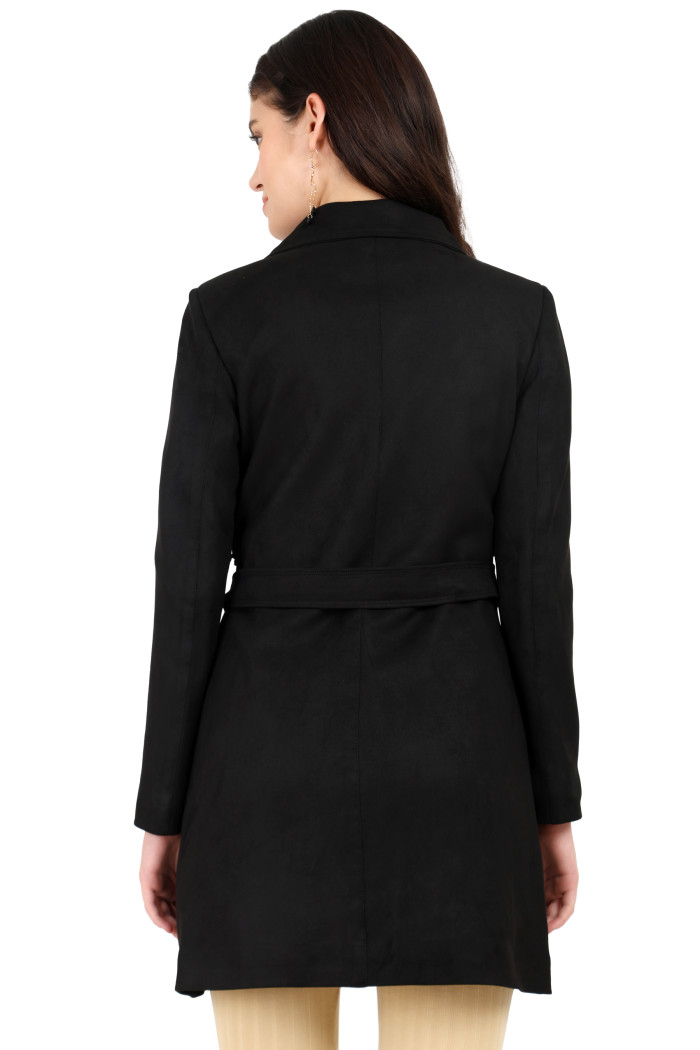 A back pose of a standing woman wearing Coatsnmore’s black double-breasted trench coat with a belt and skin bell bottom.