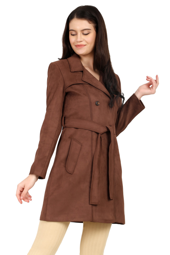 A woman is giving a standing side pose, wearing Coatsnmore’s coffee double-breast trench coat with a lapel collar, button closure, a belt, side pockets and skin bell bottom.