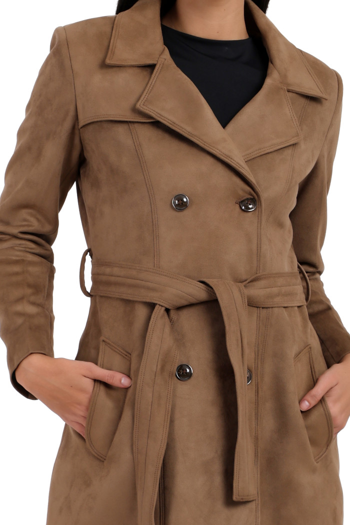 A woman in a cropped image is wearing Coatsnmore’s mouse double-breast trench coat with a lapel collar, button closure, belt and side pockets with hands in the pockets.