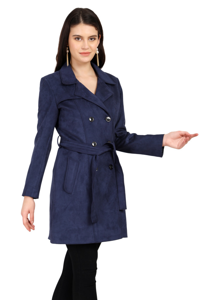 A woman is holding a standing side pose, wearing Coatsnmore’s navy double-breasted trench coat with a lapel collar, button closure, belt, side pockets, and black bottoms.