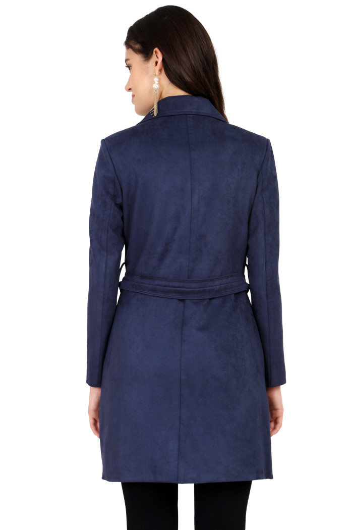 A back pose of a standing woman wearing Coatsnmore’s navy double-breast trench coat with a belt and bottom.