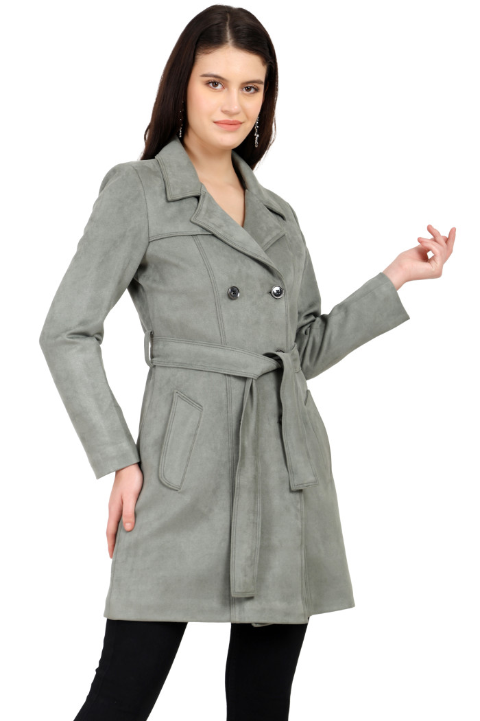 A woman is holding a standing side pose, wearing Coatsnmore’s pista double-breast trench coat with a lapel collar, button closure, belt, side pockets, and black bottoms.