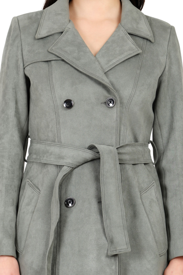 A woman in a cropped image is wearing Coatsnmore’s pista double-breast trench coat with a lapel collar, button closure, belt and side pockets.